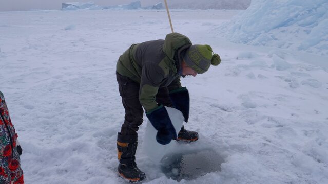 Arctic Circle sea ice subsistence - cutting block of sea ice to fish
