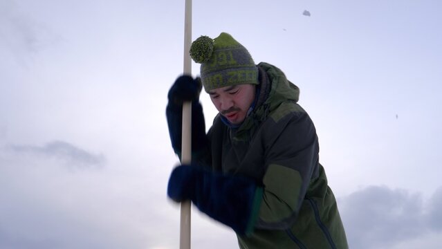 Greenland sea ice hunter: Inuit male cuts fishing hole ice