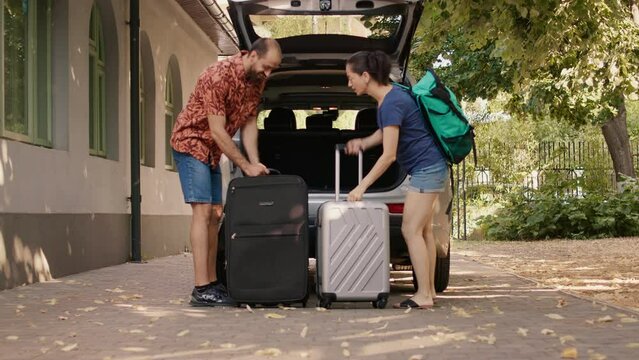 Couple loading vehicle trunk with luggage while going on marriage anniversary holiday citybreak. Married people loading car with baggage and trolleys while going on summer field trip.