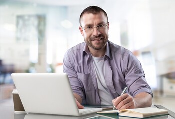 Fototapeta na wymiar Happy satisfied millennial man using laptop at office workplace, working, thinking, watching online webinar, training, making payment