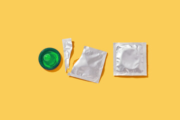 Opened and sealed condoms on yellow background.
