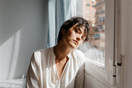 Calm non binary person leaning on window