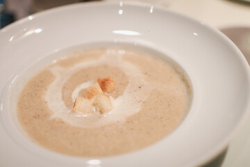 Creamy white soup with bread on top in white plate. Italian and French food. Dinner table concept.