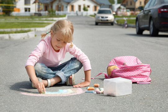 Girl drawing rainbow on road with cars