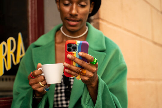 Crop man checking rainbow phone with coffee outside 