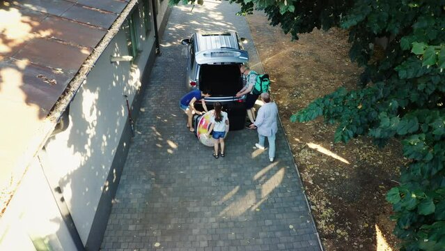 Drone shot Big casual family loading voyage luggage and trolleys inside car trunk while getting ready for summer holiday vacation. Group of people going on weekend citybreak