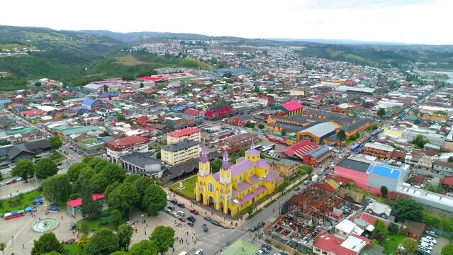 Aerial Backward Shot Of Catholic Church Amidst Houses In City Against Sky - Castro, Chile