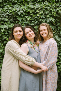 Three women standing in an embrace against  a green tree