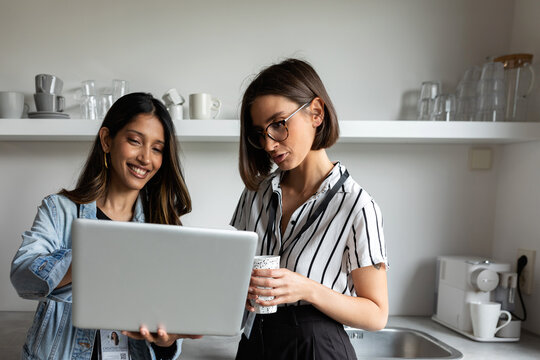 Women sharing laptop in office kitchen