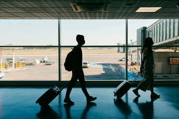 Silhouette of travelers with carry-on luggage on airport terminal