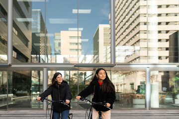 Girlfriends walking with bicycles by the city