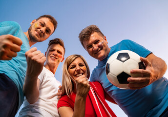 Group of ecstatic fans hugging together , view from bellow, sky background . Face paint on, fun...