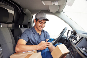 Cheerful courier scanning parcel in van