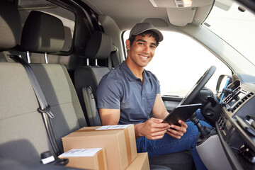 Merry delivery man with tablet sitting in van