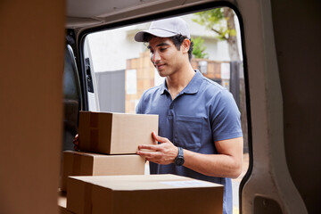 Positive delivery man taking parcel from van trunk
