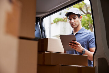 Male courier reading data on tablet near van