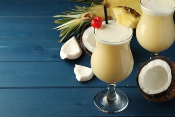 Tasty Pina Colada cocktails and ingredients on blue wooden table, space for text