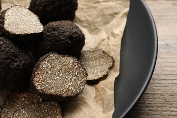 Whole and cut black truffles with parchment on plate, closeup