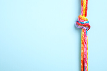 Top view of colorful ropes tied together on light blue background, space for text. Unity concept