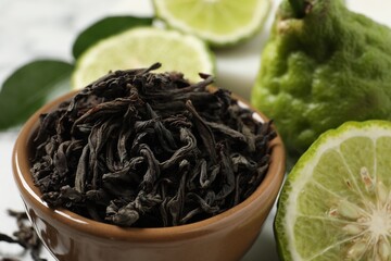 Dry bergamot tea leaves in bowl and fresh fruits on table, closeup
