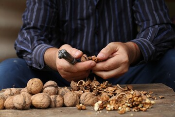 Man cracking walnuts at wooden table, closeup