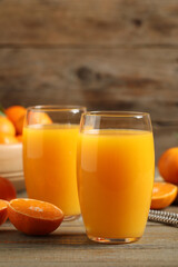 Glasses of fresh tangerine juice and fruits on wooden table