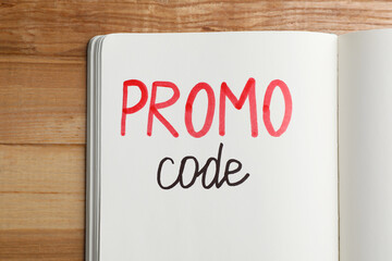 Notebook with words Promo Code on wooden table, top view