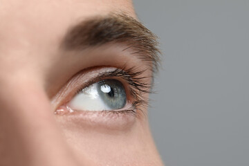 Closeup view of young man with beautiful eyes on grey background