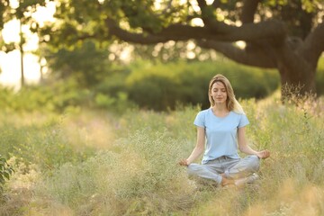 Young woman meditating on green grass in park, space for text