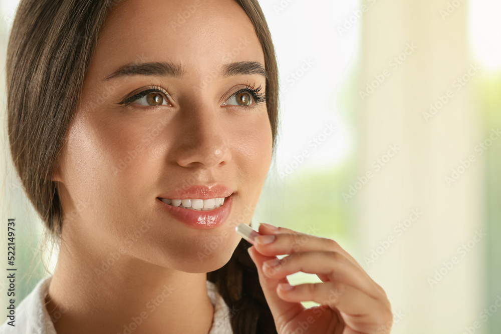 Poster Young woman taking dietary supplement pill on blurred background, closeup. Space for text