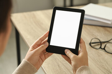 Young woman using e-book reader at wooden table indoors, closeup