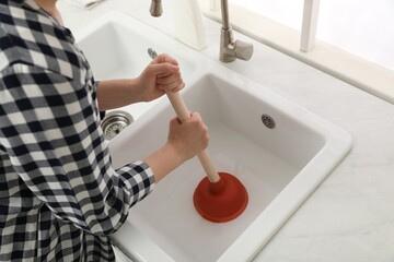 Fototapeta na wymiar Woman using plunger to unclog sink drain in kitchen, closeup