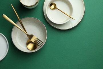 Stylish empty dishware and golden cutlery on green background, flat lay. Space for text