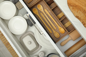 Open drawers of kitchen cabinet with different dishware and utensils, top view