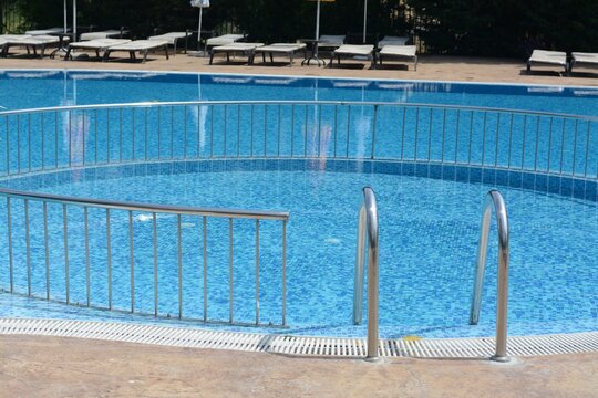 Outdoor swimming pool with ladder and railing on sunny day