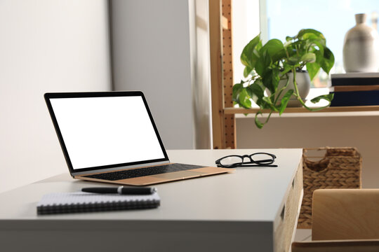 Workplace with modern laptop and glasses on white table. Mockup for design