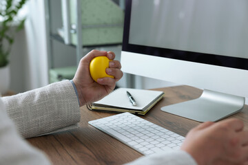 Man squeezing antistress ball while working with computer in office, closeup - obrazy, fototapety, plakaty