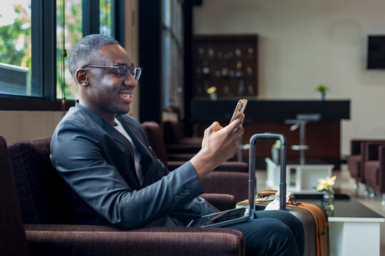 African American businessman is using mobile phone for video call while waiting in airline business departure lounge waiting for boarding the airplane
