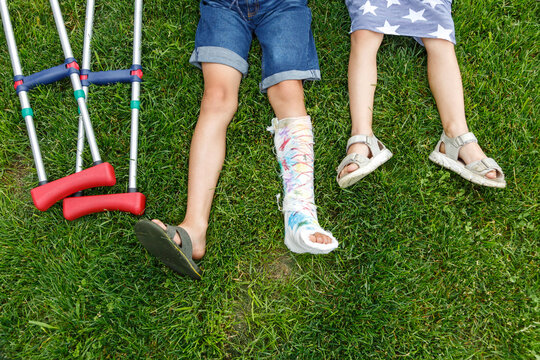 Crop kids with crutches resting on lawn