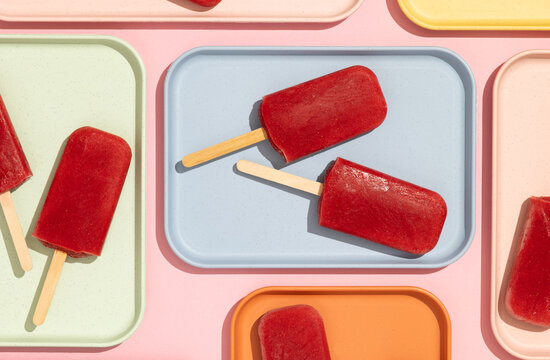 Homemade strawberry ice cream popsicles on colorful trays