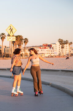 Gen Z woman and non-binary person holding hands and skating at sunset