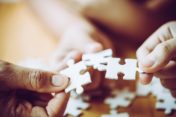 Hands of a person little child and parent playing jigsaw puzzle piece game together on wooden table...