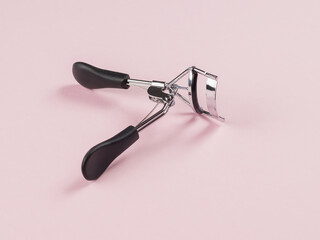 Eyelash curlers on a light pink background.