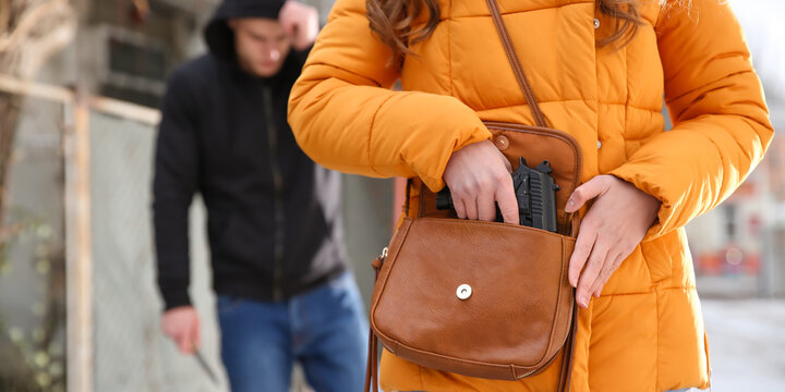 Woman taking pistol out of her bag in order to protect herself against thief