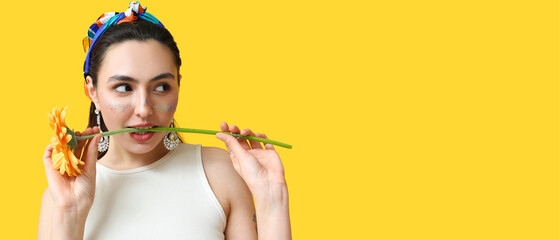 Fashionable woman with glitters on face holding flower against yellow background with space for text