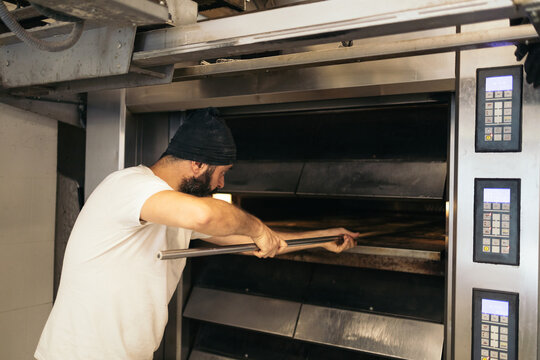 Bread maker removing the freshly baked bread from the oven