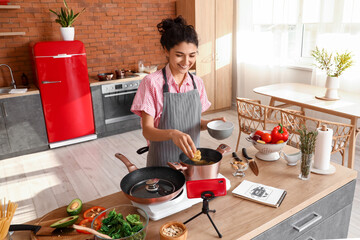 Young woman cooking pasta while watching video tutorial in kitchen