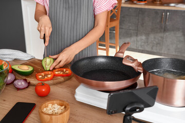 Young woman cutting avocado while following video tutorial in kitchen, closeup