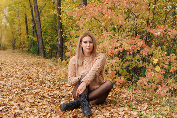 A beautiful young woman sitting in a forest on a dry autumn leaves.