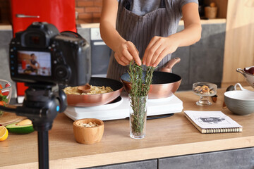 Young woman taking rosemary while recording video class in kitchen, closeup